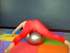 Regina Noir, en mogen kvinna, utövar yoga i ett gym medan hon bär en röd trikot, yogastrumpbyxor och är rakad